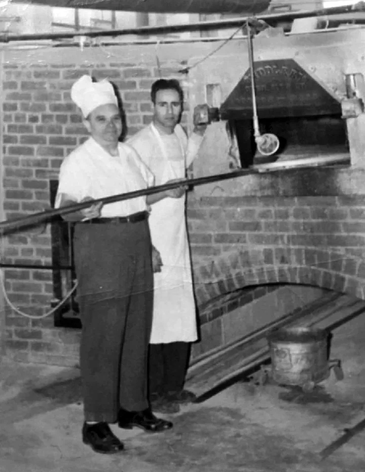 Two bakers in white at the brick oven, in a vintage black-and-white photo
