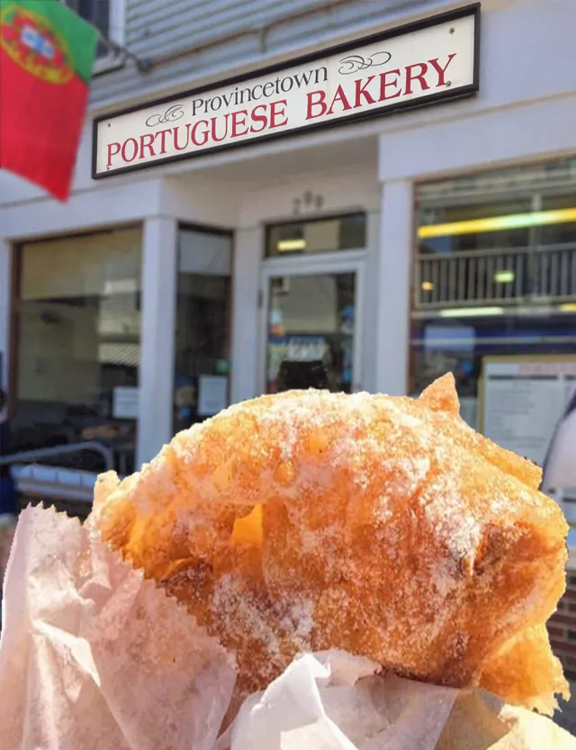 A sugar-dusted malassada held up in front of the bakery's sign